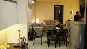 Un espace de vie compact comprenant un canapé, une table à manger, des chaises, un réfrigérateur et un coin cuisine.