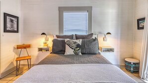 Een slaapkamer met een bed, nachtlampjes, een raam, een stoel en een klein tafeltje.