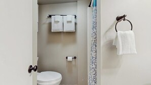 Ein Badezimmer mit Toilette, zwei Handtüchern an einem Handtuchhalter, einer Duschvorhang und einem Handtuchring.