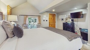 Ein Schlafzimmer mit einem großen Bett, einem Fernseher, einem Schreibtisch und einem Fenster mit Vorhängen.