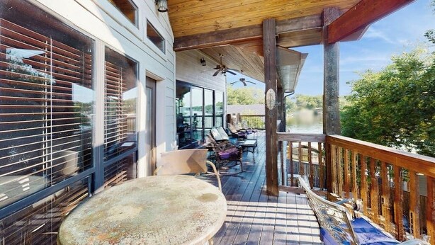 Una terraza de madera con mobiliario exterior, una mesa y un ventilador de techo.