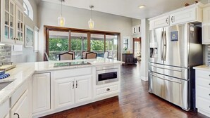 Una cocina moderna con armarios blancos, una isla grande, electrodomésticos de acero inoxidable e iluminación colgante.