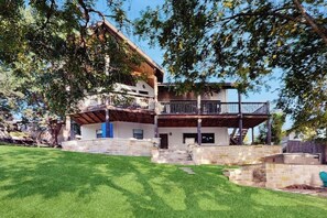 Une maison à deux étages, avec des fondations en pierre, une terrasse en bois et un escalier menant à un balcon situé au deuxième étage.