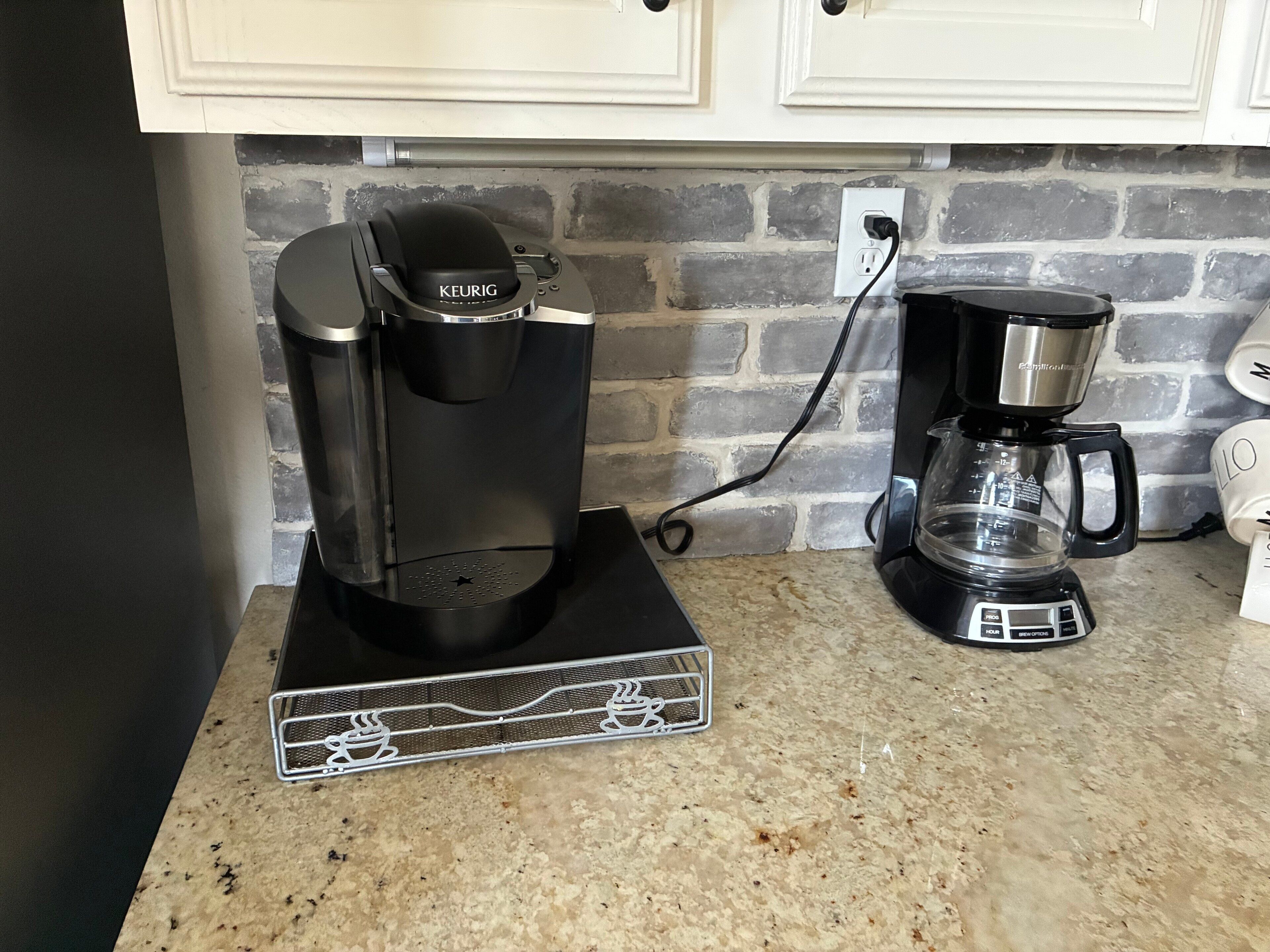 Une machine à café et une cafetière posées sur un comptoir, avec un mur de briques en arrière-plan.