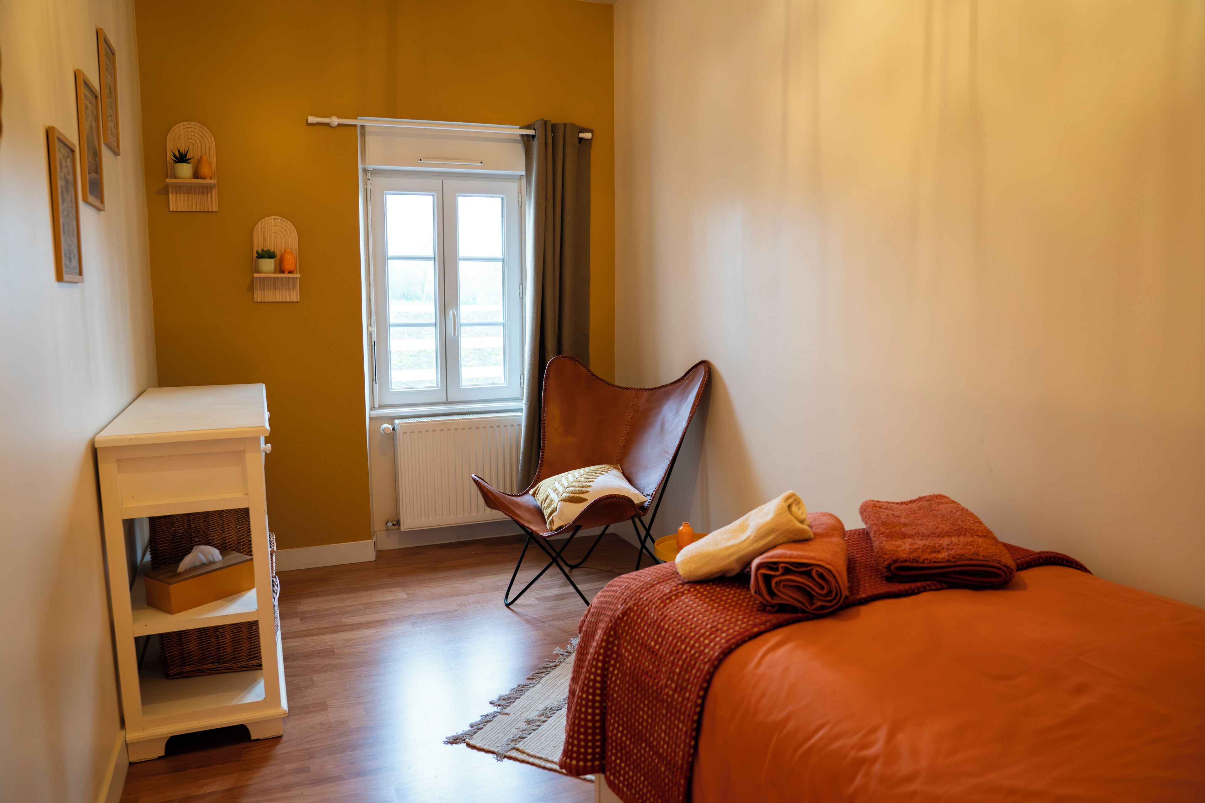 A room with a bed, a chair, a small table, and a window with curtains.