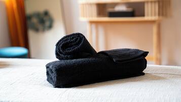 Un asciugamano nero piegato ordinatamente su un letto con lenzuolo bianco.