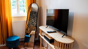 A room with a TV, a blue ottoman, a mirror, and a window with curtains. - Le50300 Gîte for 5 pers in Avranches, close to Mont Michel ! (Avranches)