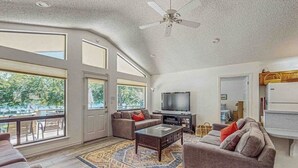 Uma sala de estar ampla com uma televisão grande, assentos confortáveis e vista através das portas de vidro.