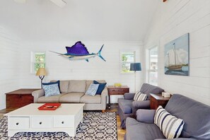A living room with a sofa, coffee table, patterned rug, and wall art including a fish and a sailboat. - Lakefront home on water with great views, boat dock, al fresco dining, and WiFi (Kingsland)