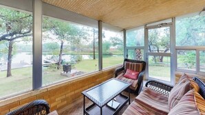 En inglasad uteplats med möbler i rotting, stora fönster och utsikt över en trädgård.