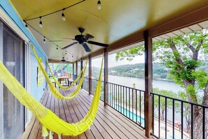 A wooden deck with a hammock, a ceiling fan, and a view of a lake. - Mid-century modern lake house w/private waterfront pool & boat dock (Marble Falls)