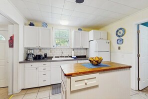 Eine Küche mit weißen Schränken, einer Holz Arbeitsplatte, einer Spüle und einem Kühlschrank.