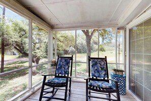Eine überdachte Veranda mit zwei Schaukelstühlen, einem kleinen Tisch und einem Blumentopf.
