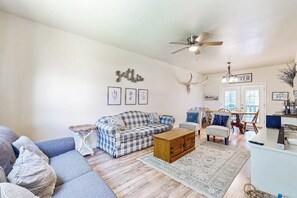 A living room with a sofa, a coffee table, a rug, a ceiling fan, and a wall-mounted decoration.