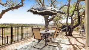 A wooden deck with a table and chairs, an umbrella, and a hammock. - Cliffside Oasis | Deck + Dock | Shuffleboard (Spicewood)