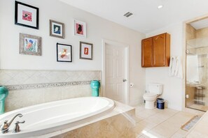 Une salle de bain avec une baignoire, des toilettes, une douche et des tableaux encadrés au mur.