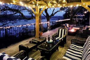 Une terrasse extérieure avec des meubles en osier, une table à plateau de verre et des guirlandes lumineuses.