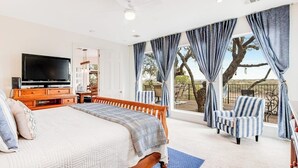A bedroom with a large bed, a TV, a balcony with chairs, and curtains. - Cliffside Oasis | Deck + Dock | Shuffleboard (Spicewood)