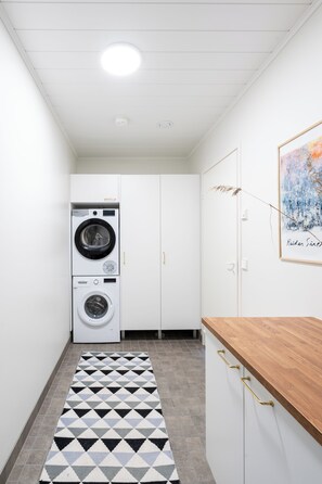 A laundry room with stacked washers and dryers, a patterned rug, and a wooden countertop. - Villa Arctic Glow with Sauna (Rovaniemi)