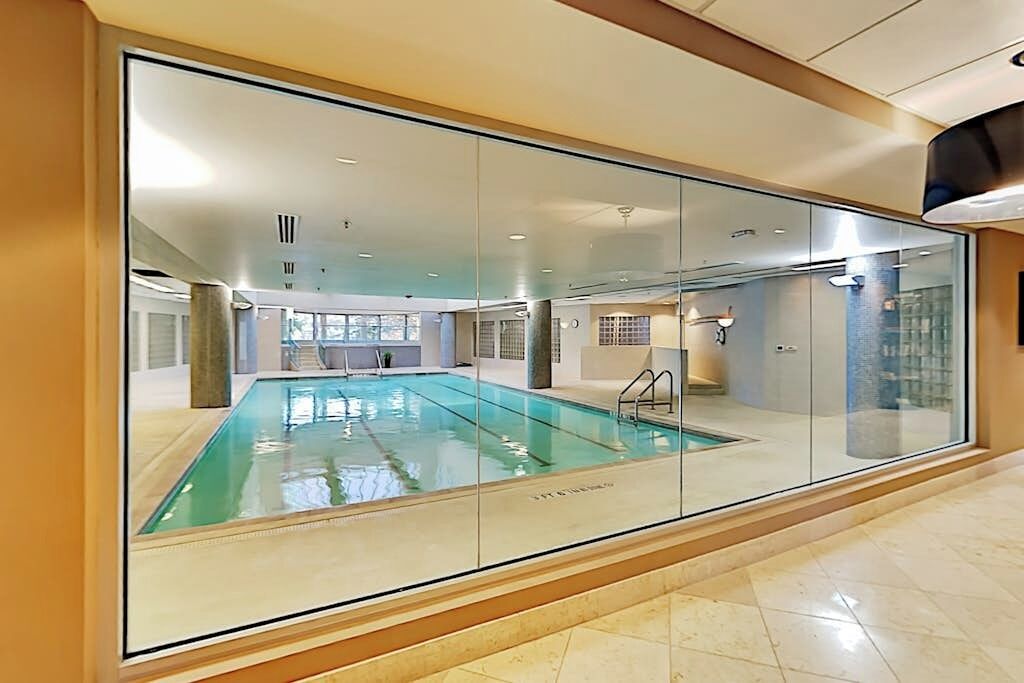 Une piscine intérieure avec des parois en verre transparent, un sol carrelé et un escalier apparent menant à un autre niveau.