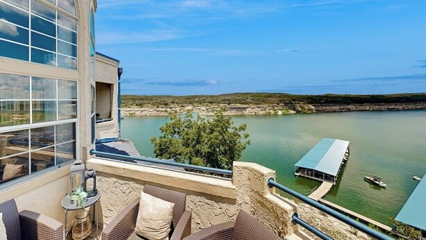 Ein Balkon mit Korbmöbeln, Blick auf einen See und eine Bootsanlegestelle.