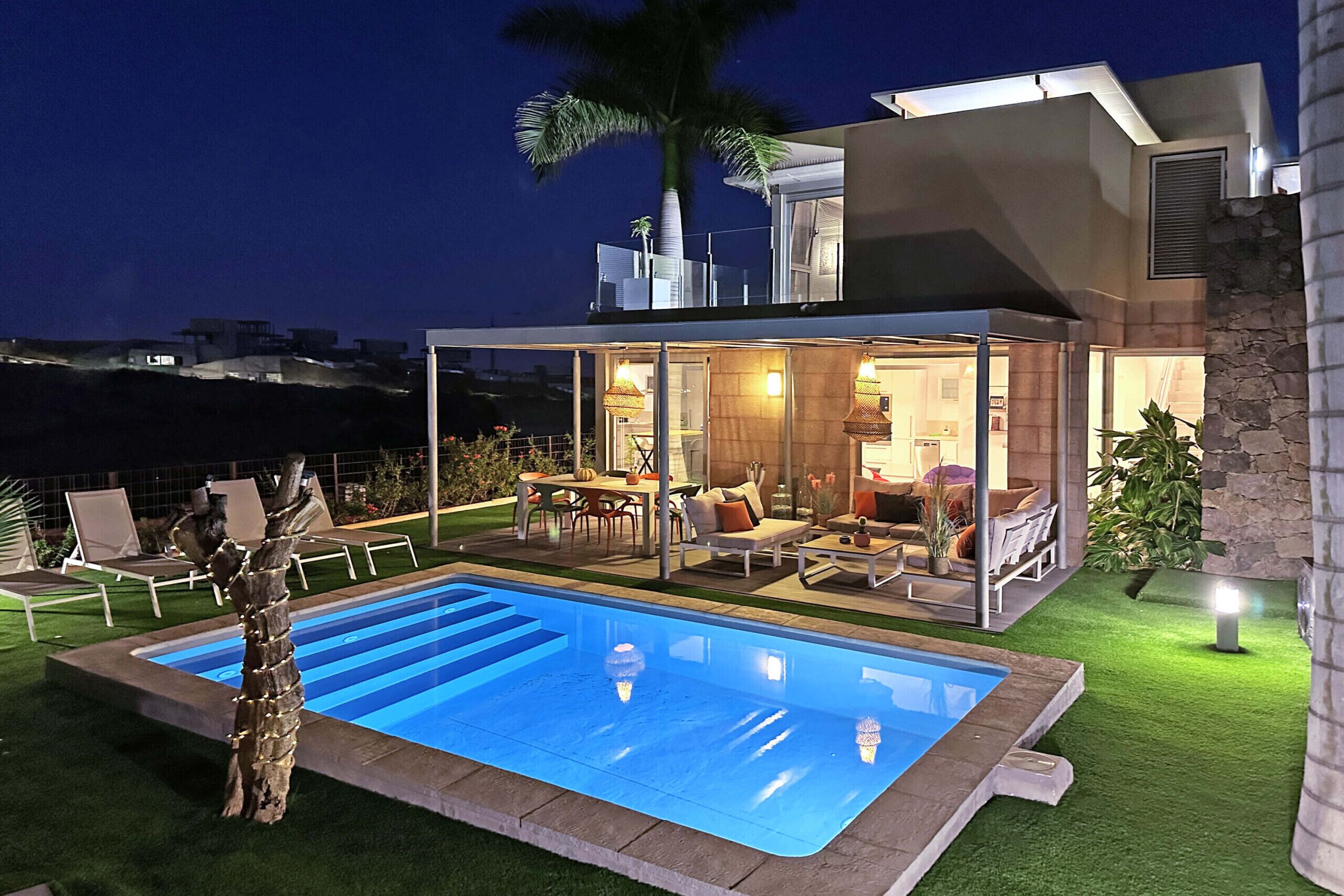 A modern house with a swimming pool, outdoor seating, and a well-lit patio area.