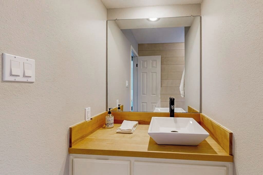 A bathroom with a white sink, a mirror, and a wooden countertop.