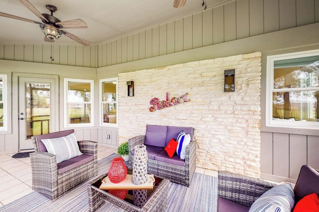 Un patio couvert aménagé avec des meubles en osier, un mur en pierre et un ventilateur de plafond.