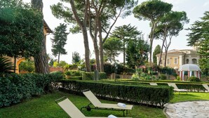 A garden with two sun loungers, a stone pathway, and a building with a dome in the background. - Vigne Franceschini Resort - villa with pool in the heart of Rome (Roma)