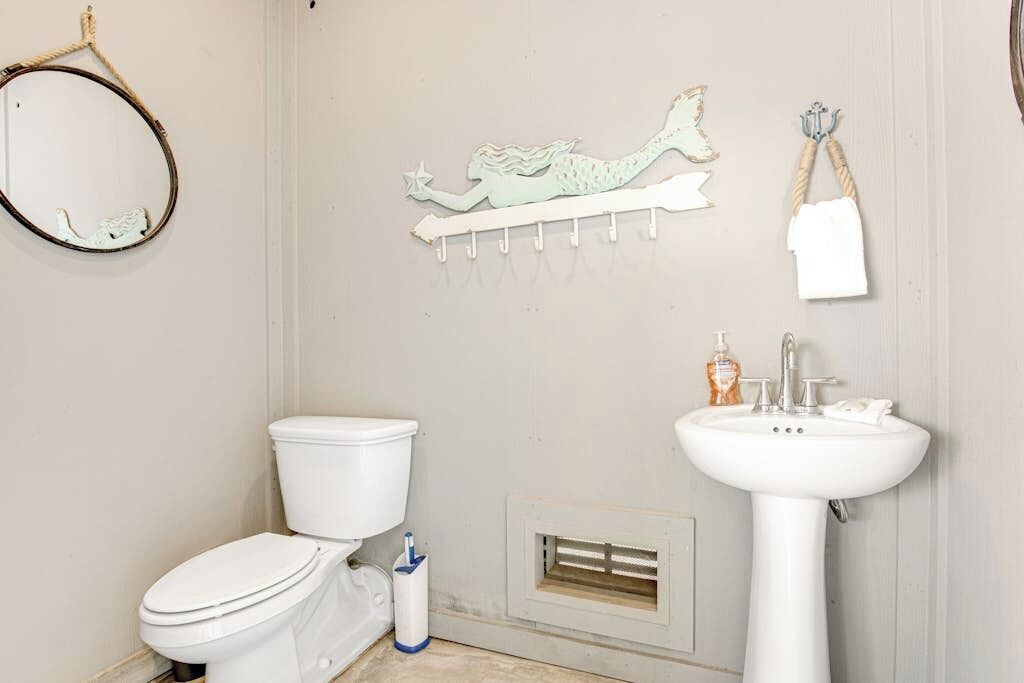 Une salle de bain équipée d’un WC, d’un lavabo, d’un miroir, d’un porte-serviettes et d’œuvres d’art décoratives sur les murs.