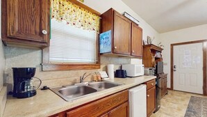 A kitchen with wooden cabinets, a double sink, a coffee maker, a microwave, and a refrigerator. - Cozy & Cute Cabin with Fenced Patio, Grill, AC & WiFi - Walkable Locale (Fredericksburg)