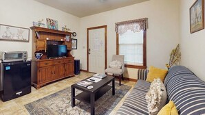A living room with a sofa, coffee table, TV, and a cabinet. - Cozy & Cute Cabin with Fenced Patio, Grill, AC & WiFi - Walkable Locale (Fredericksburg)