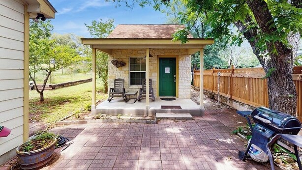 A small stone building with a porch, a green door, and two chairs. - Cozy & Cute Cabin with Fenced Patio, Grill, AC & WiFi - Walkable Locale (Fredericksburg)
