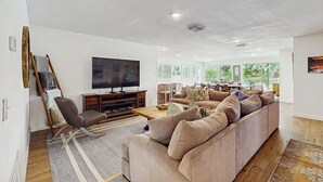 En moderne stue med et stort fladskærms-tv, en sofa, et sofabord og en lænestol.