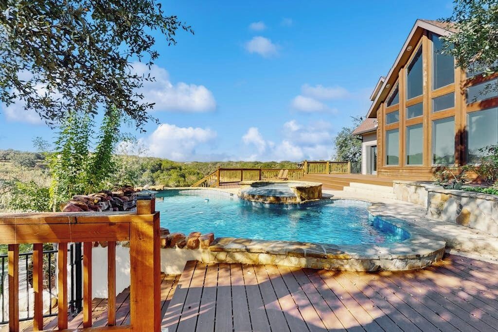 Une piscine dotée d’une terrasse en bois, d’une structure en pierre et d’un bâtiment avec de grandes fenêtres.