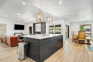 A modern kitchen with a central island, a dining area with a wooden table and chairs, and a seating area with a sofa. - Spacious & elegant haven with huge yard, updated interior, AC, & fast WiFi (Horseshoe Bay)
