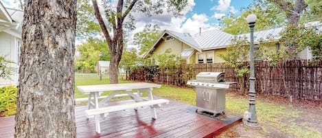 En trädgård med en träaltan, en grill och ett picknickbord.