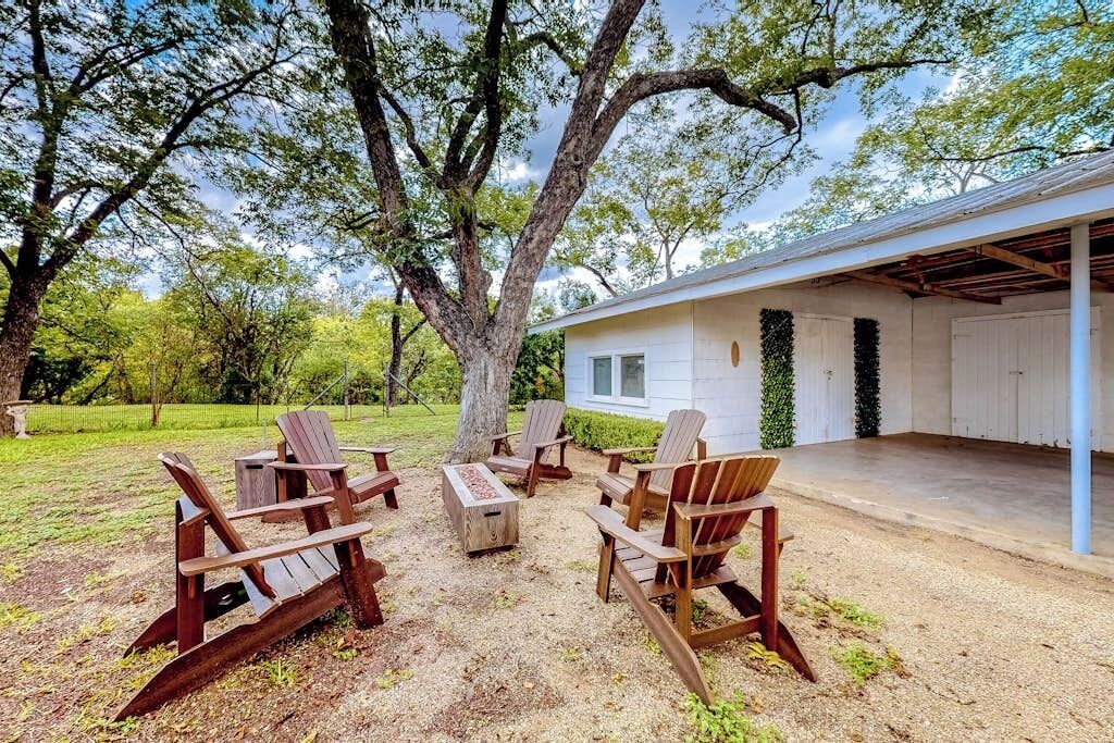 Un área de estar al aire libre con sillas Adirondack y un brasero, un patio cubierto y un edificio blanco con garaje.