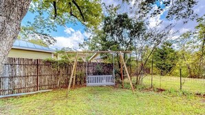 A backyard with a wooden swing set, a wooden fence, and a house in the background. - Enchanting home with fireplace, full kitchen, patio, central AC, & washer/dryer (Fredericksburg)