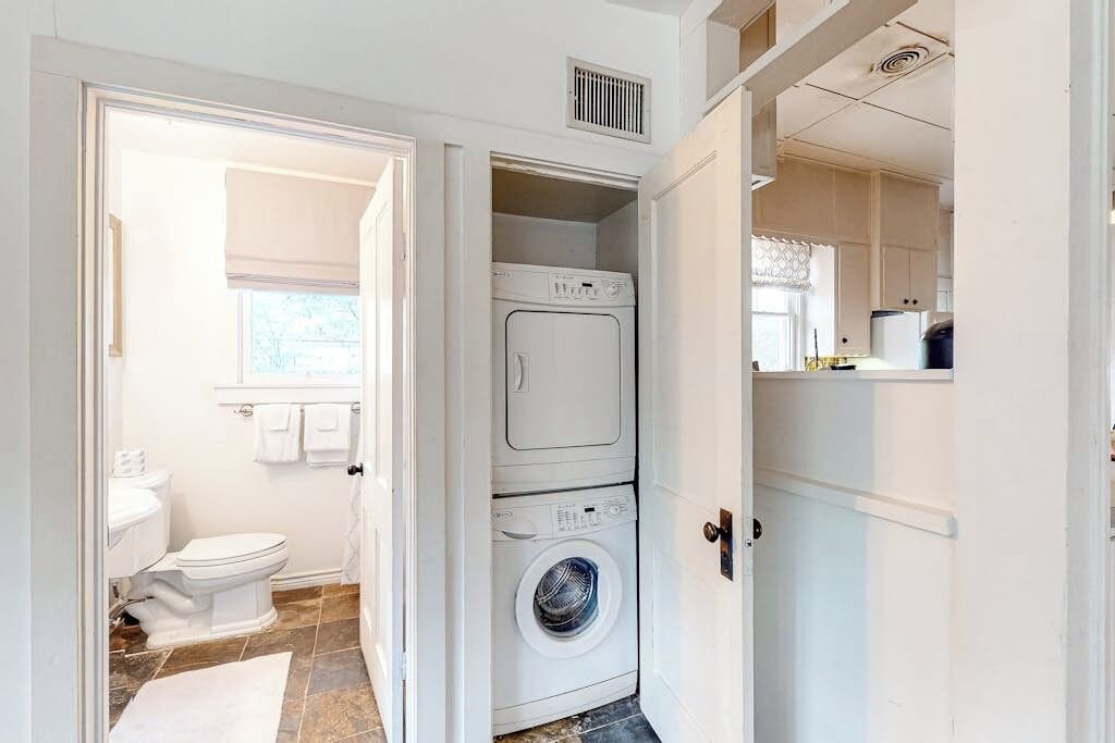 Une buanderie équipée de machines à laver et de sèche-linge superposés, de toilettes et d’une fenêtre.