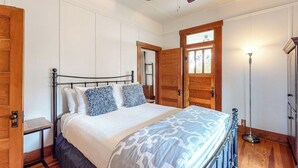 A bedroom with a bed, a ceiling fan, a wooden door, and a floor lamp. - Enchanting home with fireplace, full kitchen, patio, central AC, & washer/dryer (Fredericksburg)