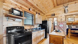 A wooden cabin interior with a kitchen featuring a stove, microwave, cabinets, and a refrigerator. - Dog-friendly gem on 11 acres w/valley views, deck, gas grill, fireplace (Fredericksburg)