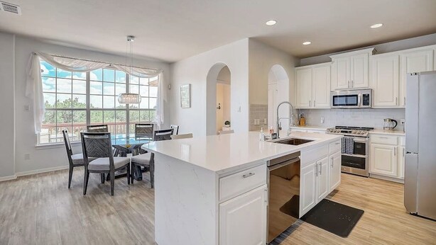 A modern kitchen with white cabinetry, a central island, and a dining area with chairs. - Spacious, dog-friendly home with two decks, views, grill, W/D & community pool (Lago Vista)