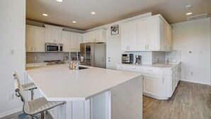 A modern kitchen with white cabinetry, a central island, stainless steel appliances, and a bar stool. - Spacious, dog-friendly home with two decks, views, grill, W/D & community pool (Lago Vista)