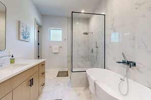 Un baño moderno con ducha envuelta en vidrio, una bañera independiente y un tocador con espejo.