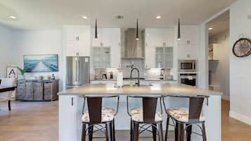 Una cocina moderna con una isla central, iluminación colgante y un comedor con taburetes de bar.