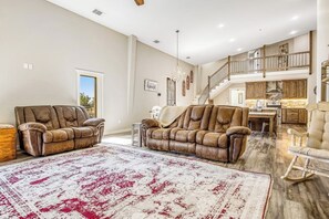 Ein geräumiges Wohnzimmer mit Ledersofas, einem großen Teppich mit Muster und einer hohen Decke mit sichtbaren Balken.