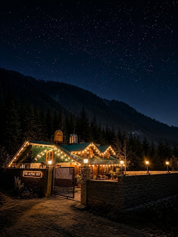 A lodge with a sign 'The Alpine Hut' at night, surrounded by trees and a starry sky.