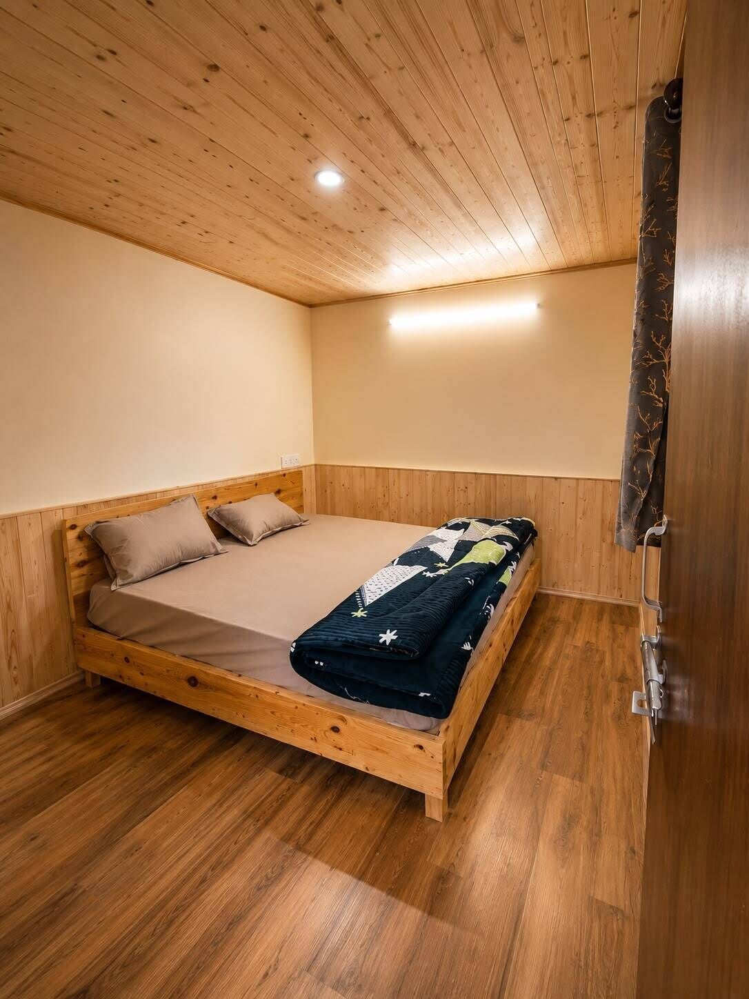 A single bed with a wooden frame and a quilt, a wooden ceiling, and a wooden floor.