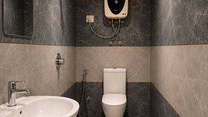 A modern bathroom with a wooden ceiling, a white sink, a toilet, and a showerhead. - The Alpine Hut (Manali)